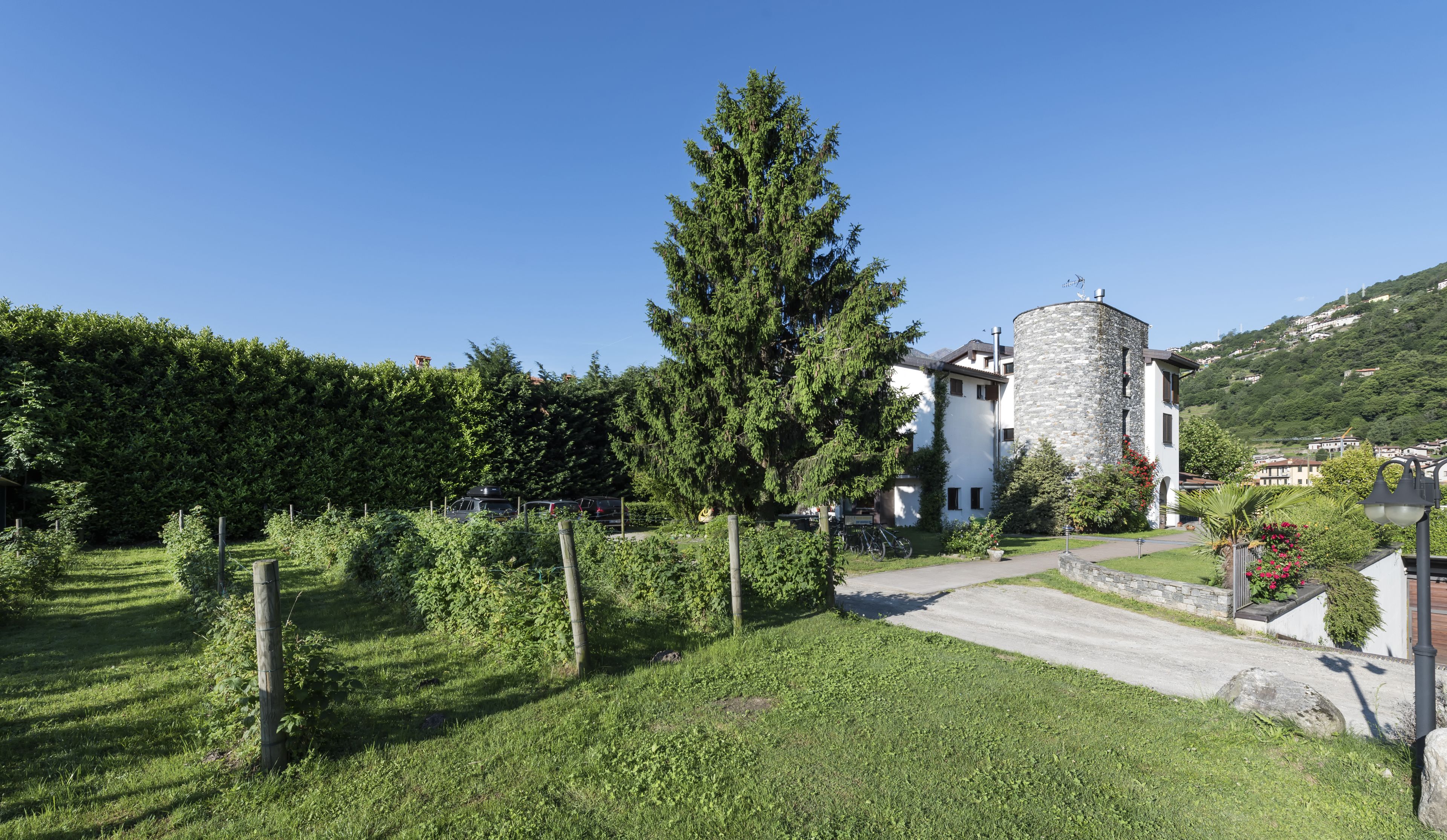 A building with a stone tower, surrounded by lush greenery and a clear blue sky.