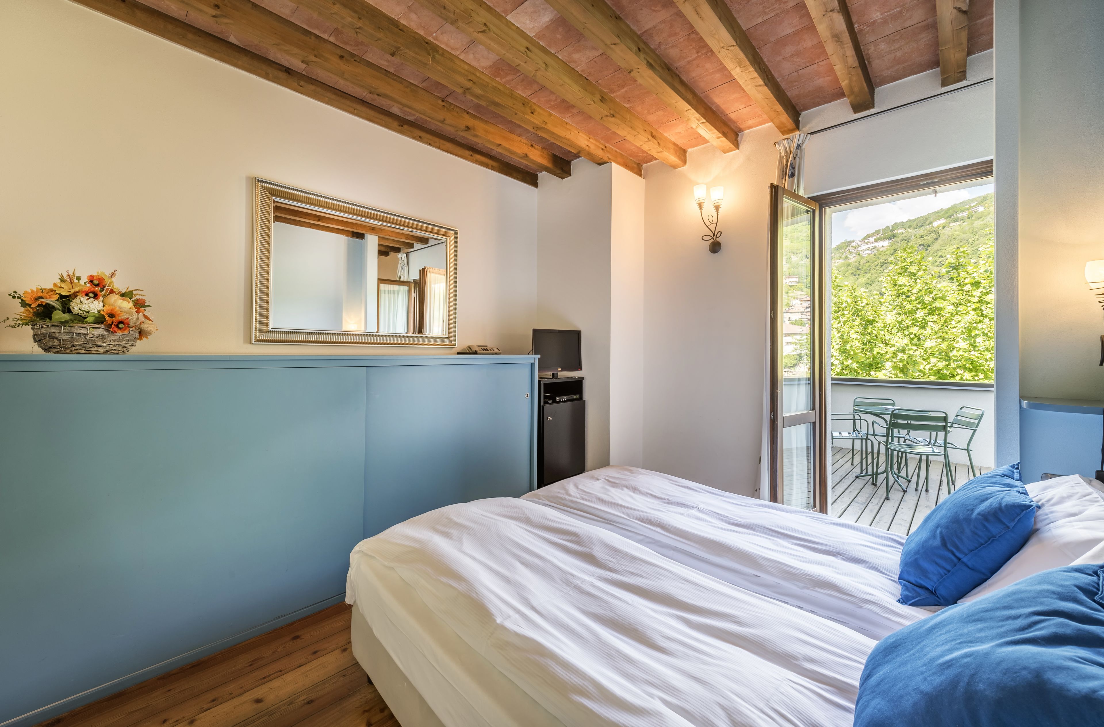 A bedroom with a bed, a dresser, a mirror, a window, and a balcony with chairs.