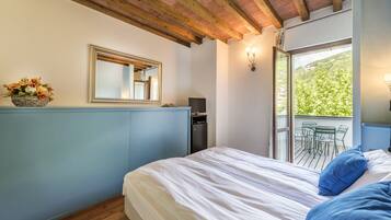A bedroom with a bed, a dresser, a mirror, a window, and a balcony with chairs.