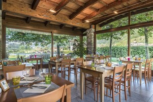 A restaurant with wooden tables and chairs, large windows, and a stone pillar.
