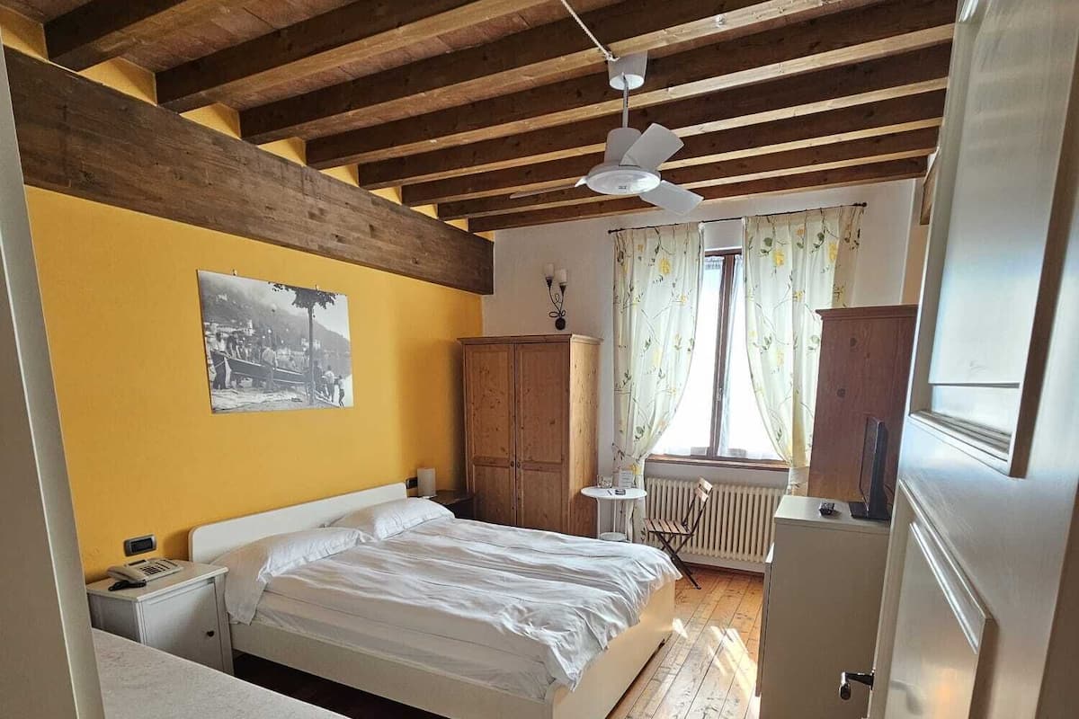 Ein Schlafzimmer mit Holzboden, einem Bett, einem kleinen Nachttisch, einem Heizkörper und einem Fenster mit Vorhängen.