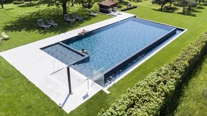 Ein rechteckiger Swimmingpool mit einer gefliesten Liegefläche, umgeben von gepflegtem Rasen und Bäumen.