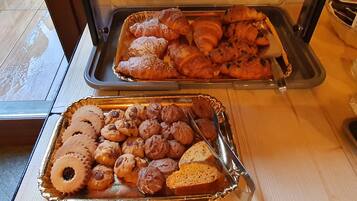 Bandejas de pasteles que incluyen croissants y galletas sobre una mesa.