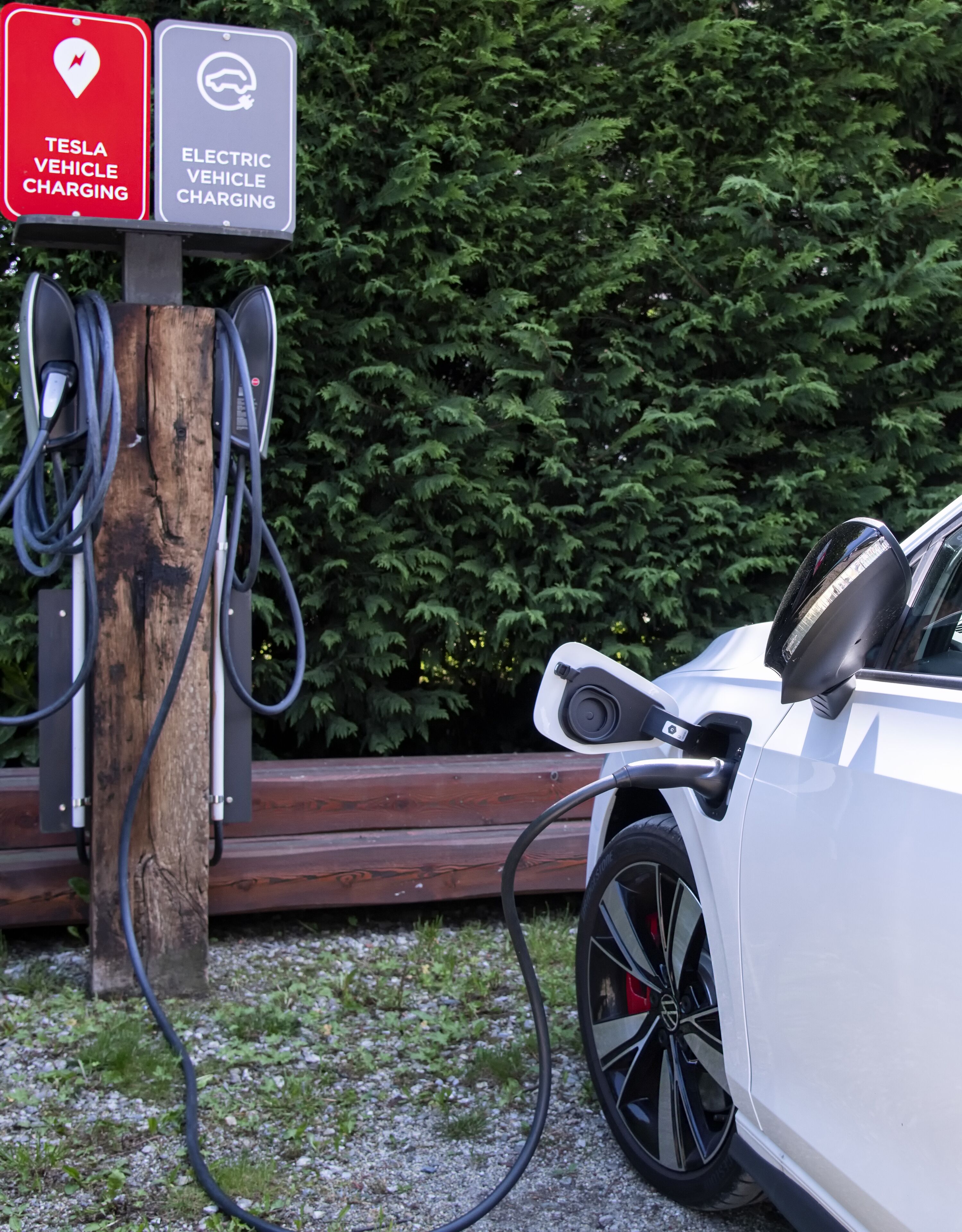 A Tesla vehicle charging at a station with a sign indicating electric vehicle charging.