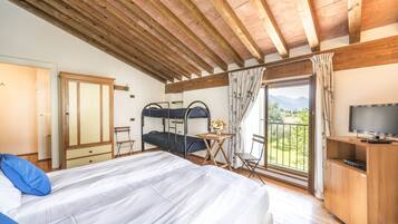 Une chambre avec un lit, des poutres en bois au plafond, un bureau, une chaise, une télévision et un balcon offrant une vue sur les montagnes.