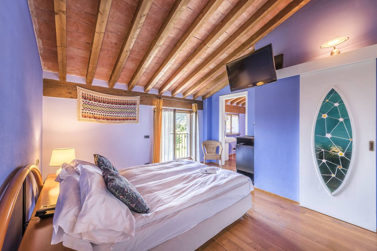 Ein Schlafzimmer mit Holzbalkendecke, einem Bett mit weißen Bettwäsche, einem darüber angebrachten Fernseher und einer Wanddekoration.