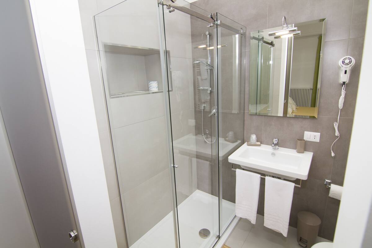 Een moderne badkamer met een douchecabine van glas, een witte wastafel en een spiegel erboven.