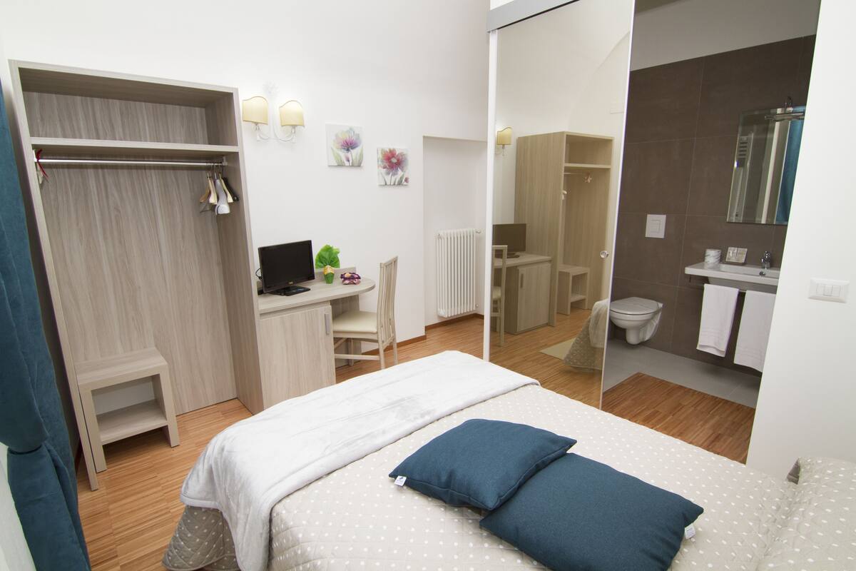 Een slaapkamer met een bed, een bureau en een stoel. Uitzicht op een inloopkast en een badkamer door een geopende deur.