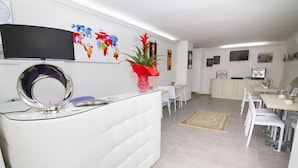 A modern kitchen with white cabinetry, a coffee machine, and a dining area with white chairs and a table. - Al Bastione Relais (Gravina in Puglia)