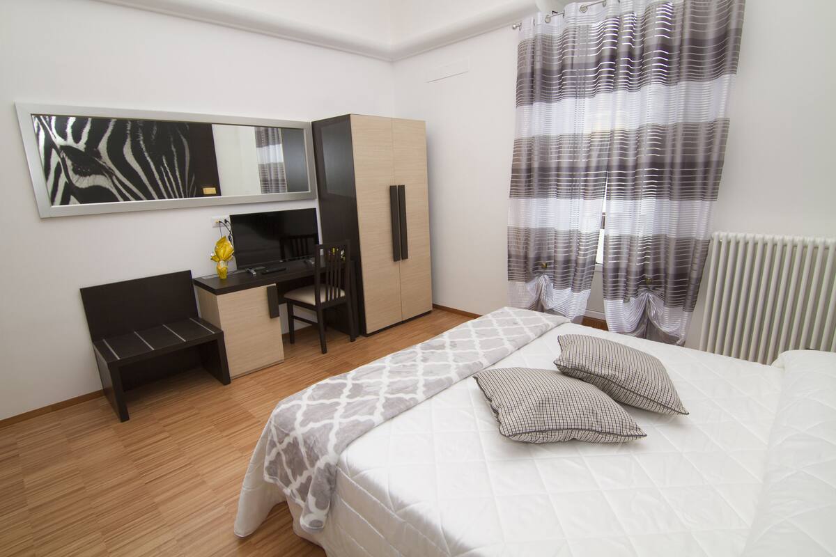 Een hotelkamer met een bed, bureau, stoel, kledingkast en een grote spiegel.