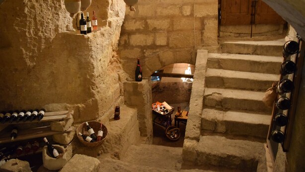 A stone-walled cellar with wine bottles on shelves and a wooden chest. - Al Bastione Relais (Gravina in Puglia)