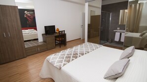 A modern bedroom with a large bed, a wardrobe, a desk with a chair, a TV, and a bathroom with a shower and mirror. - Al Bastione Relais (Gravina in Puglia)