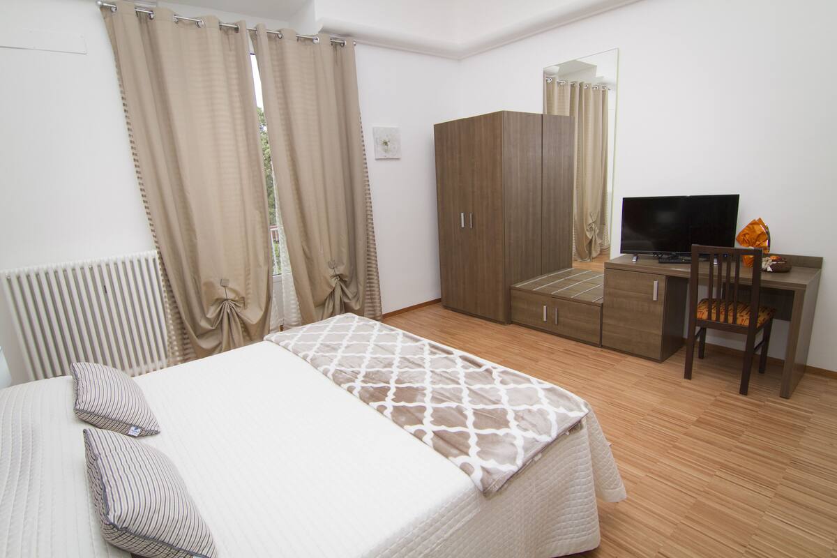 Een slaapkamer met een bed, een kledingkast, een bureau met stoel en een televisie.