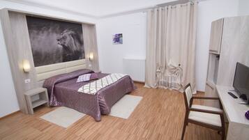 Ein Schlafzimmer mit einem Bett, einem Schreibtisch, einem Sessel, einem Fernseher und einem großen Gemälde an der Wand.