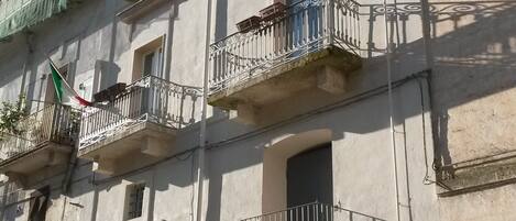 Un edificio de varios pisos con balcones, una entrada visible con el rótulo "AL BASTION" y una bandera.
