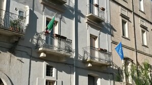 A multi-story building with balconies, a flag, and parked cars. - Al Bastione Relais (Gravina in Puglia)