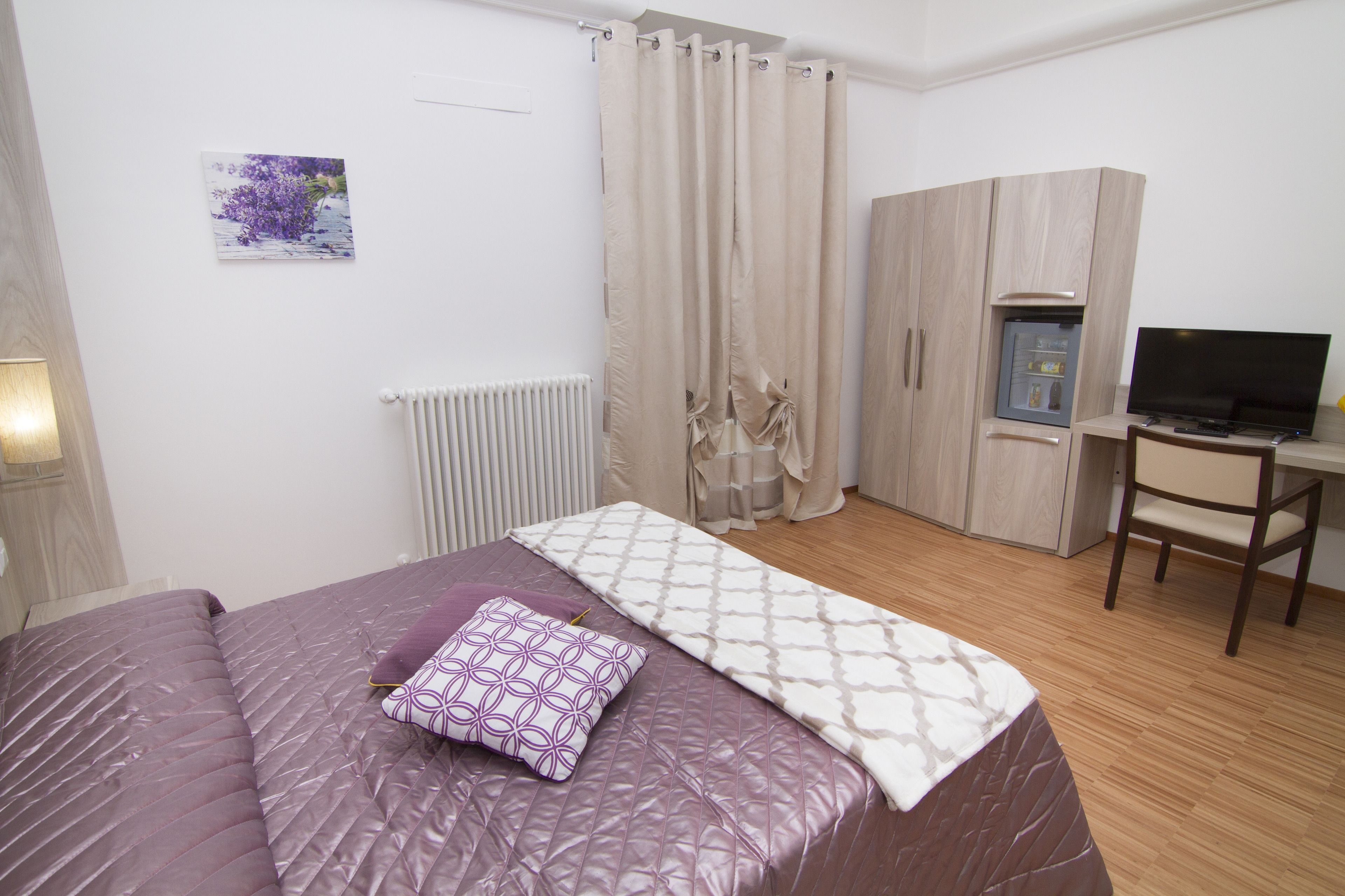 A bedroom with a bed, a desk, a chair, a radiator, a wardrobe, and a television.