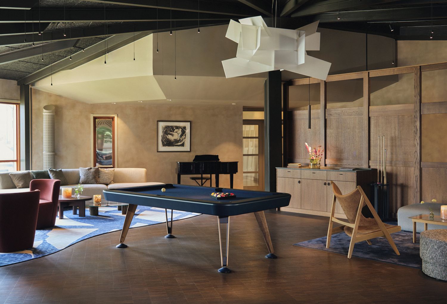 Ein modernes Wohnzimmer mit Billardtisch, einer Couch, einem Klavier und einer großen abstrakten Skulptur.