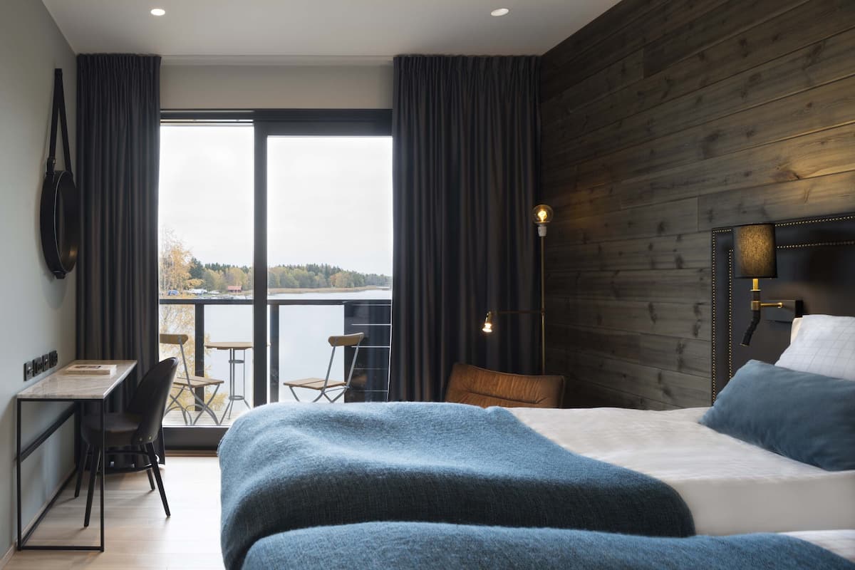 Quarto com uma cama grande, uma escrivaninha com cadeira e vista para a água através de uma porta de correr.