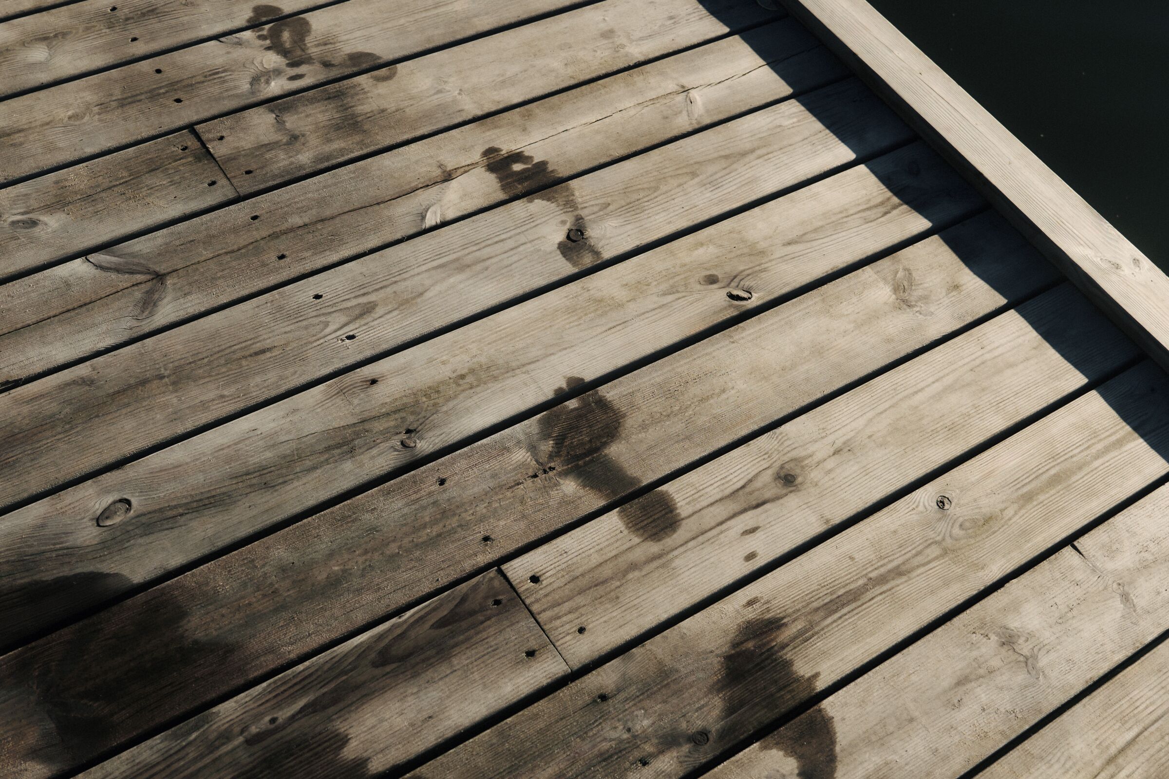 Een houten terras met duidelijke slijtage, inclusief vlekken en gaten.