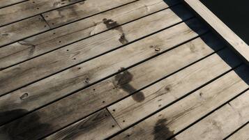 Een houten terras met duidelijke slijtage, inclusief vlekken en gaten.