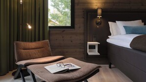 Un dormitorio moderno con una cama grande, una mesita de noche, un sillón de lectura y una ventana con cortinas.