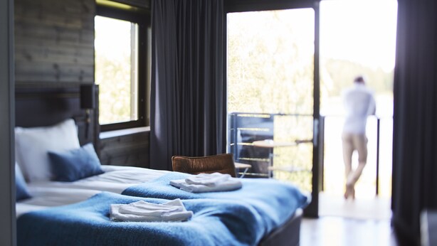 Habitación de hotel moderna con una cama grande, una silla y un balcón con vistas al exterior.