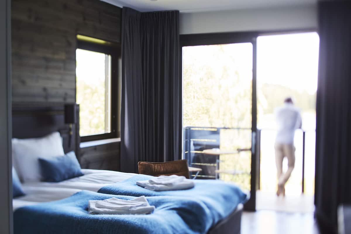 Quarto de hotel moderno com uma cama grande, uma cadeira e varanda com vista para o exterior.