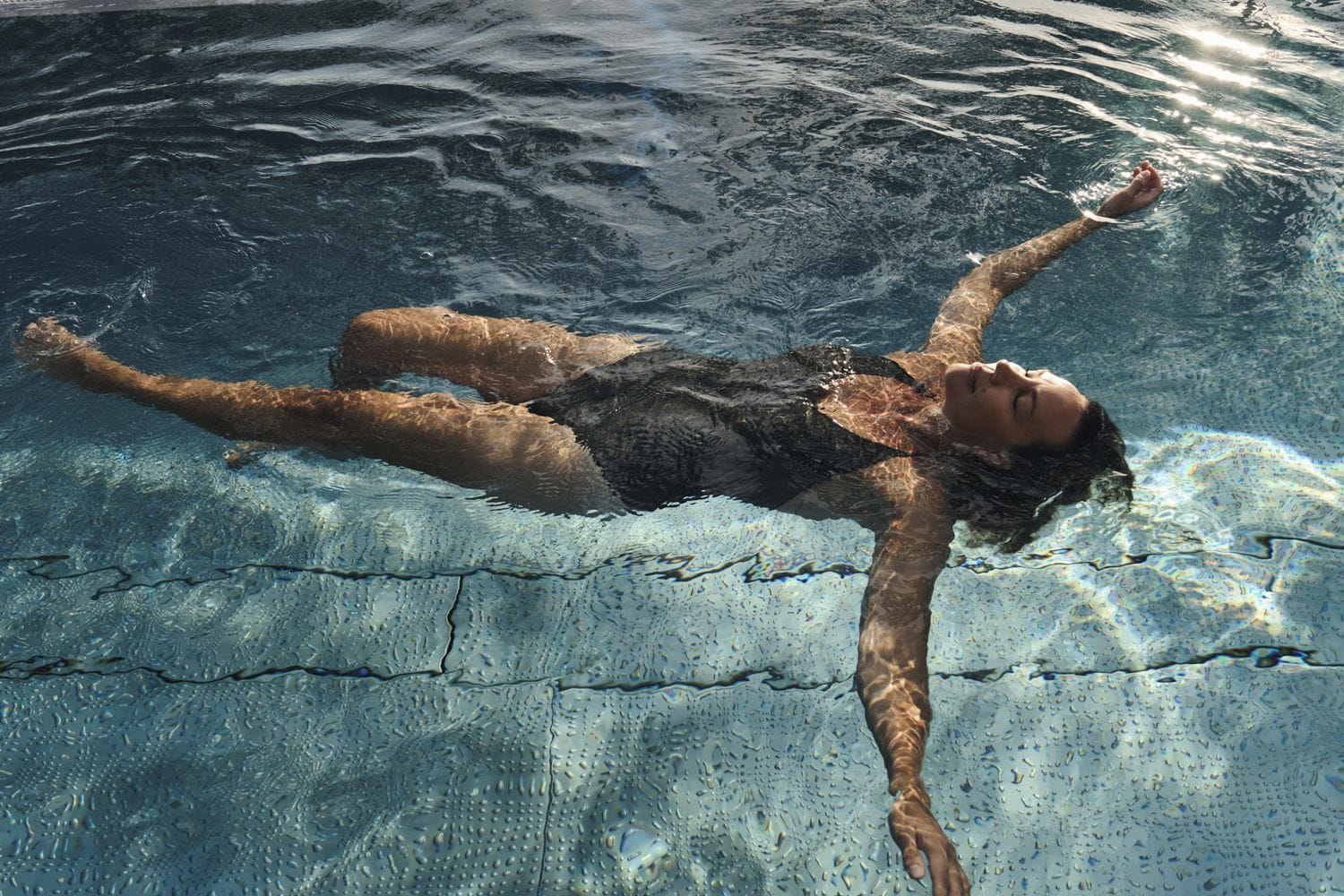 A person floating in a pool with clear water and a visible lane divider.