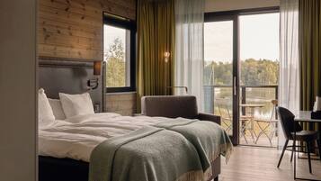 A bedroom with a bed, a chair, a table, and a balcony with a view of a lake.