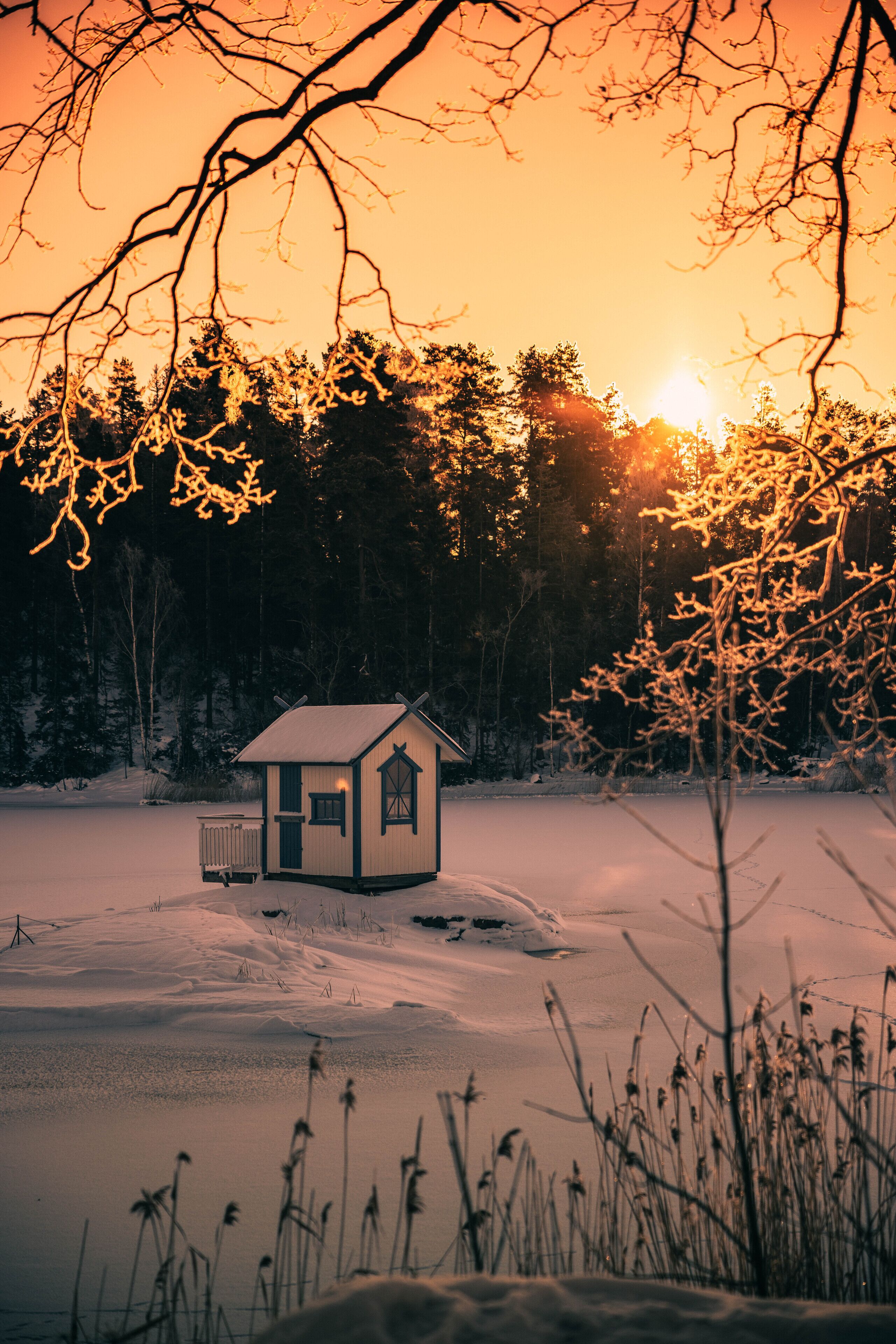 Pieni mökki, jossa on kalteva katto ja savupiippu, ja sen ympärillä on lumipeitteistä maastoa ja puita.