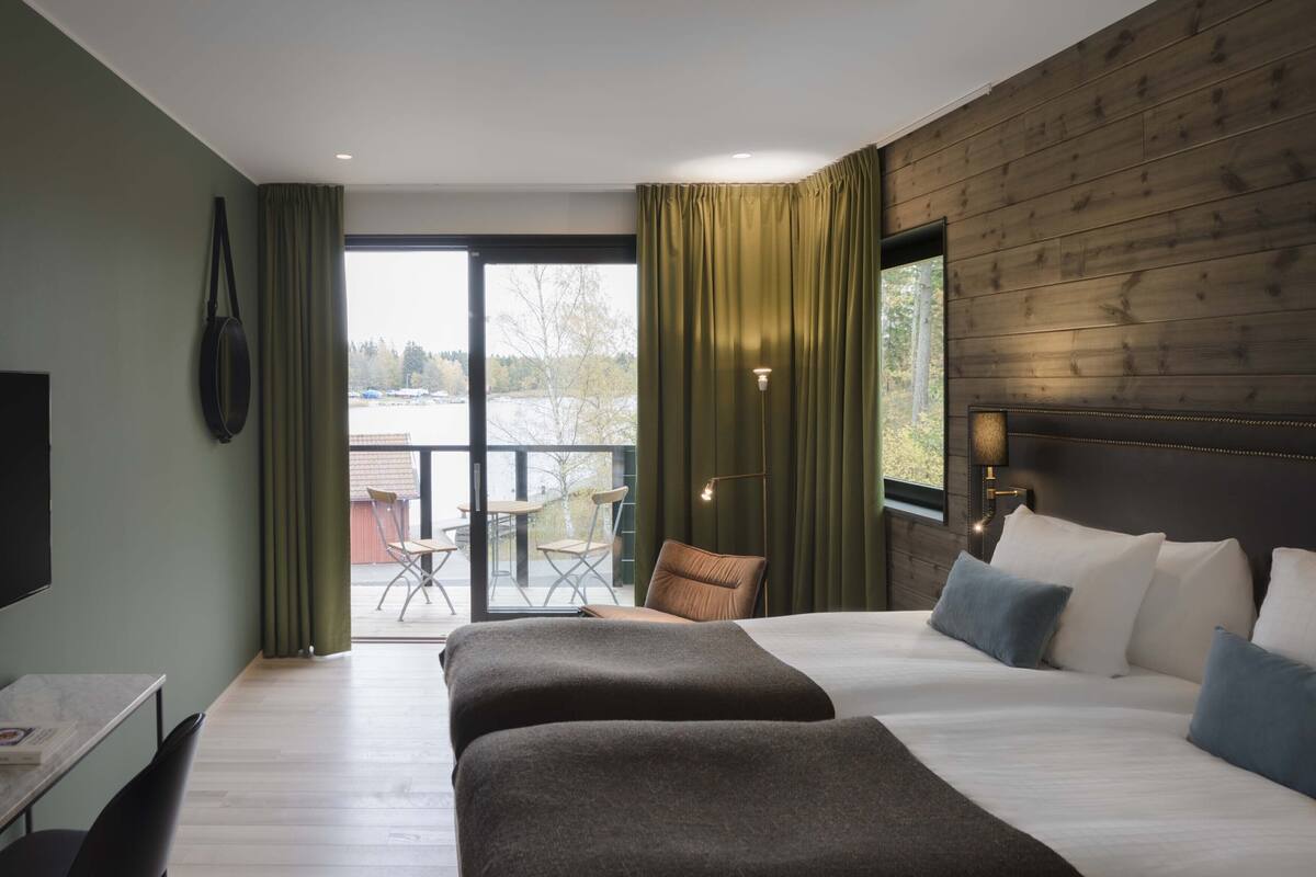 Quarto de hotel com uma cama grande, uma mesa, uma cadeira e vista para o exterior.