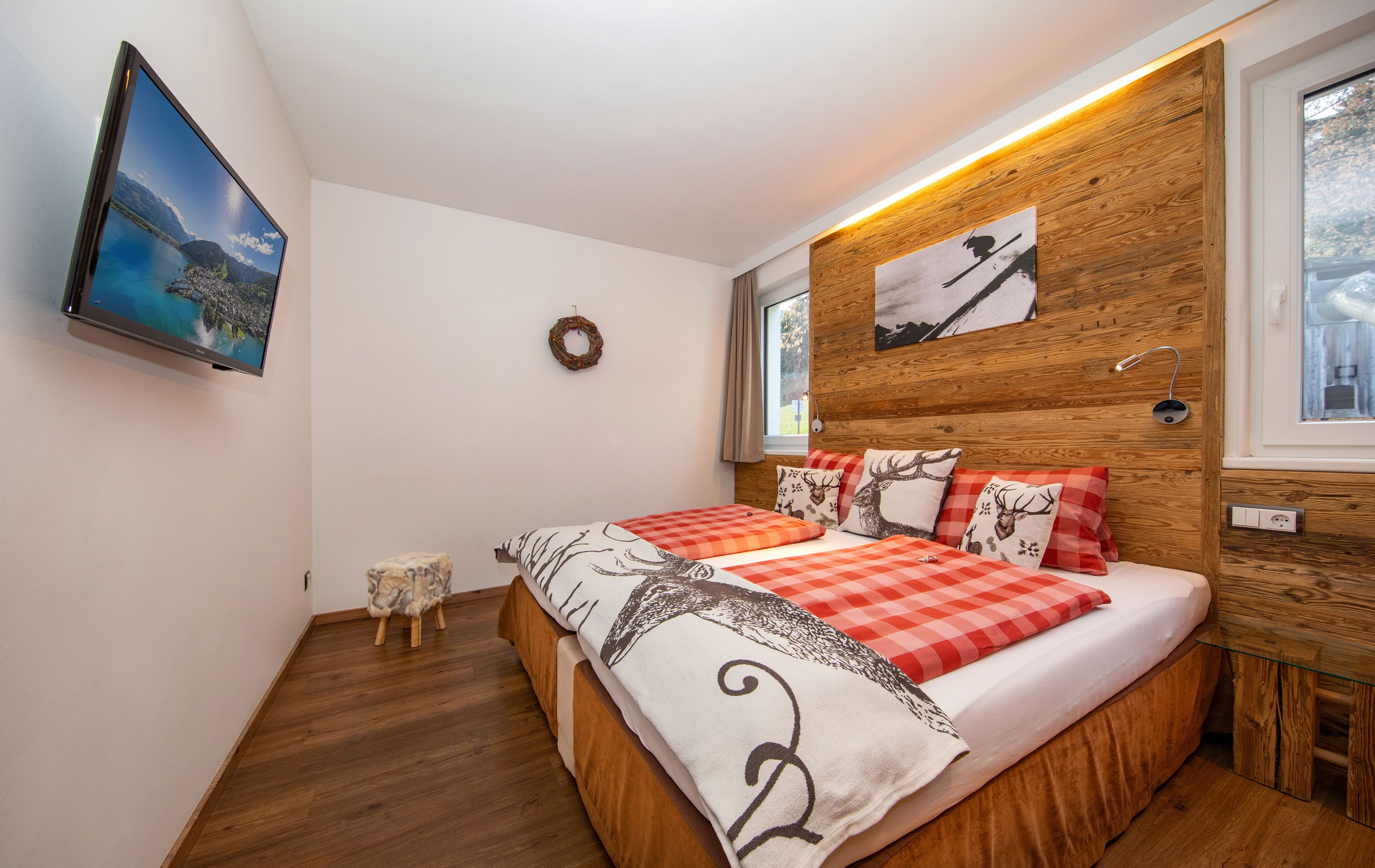 Een slaapkamer met een houten hoofdeinde, een bed met rood-wit geblokt beddengoed, een wandgemonteerde televisie en een ingelijst schilderij aan de muur.