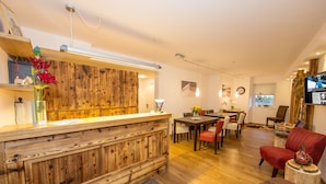 A wooden reception desk with a modern light fixture, a dining area with chairs and a table, and a red armchair. - Living Schönwies (Zell am See)