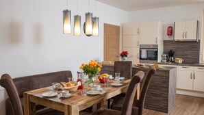 A modern kitchen with white cabinets, a wooden island, and a dining area with a wooden table and brown chairs. - Living Schönwies (Zell am See)