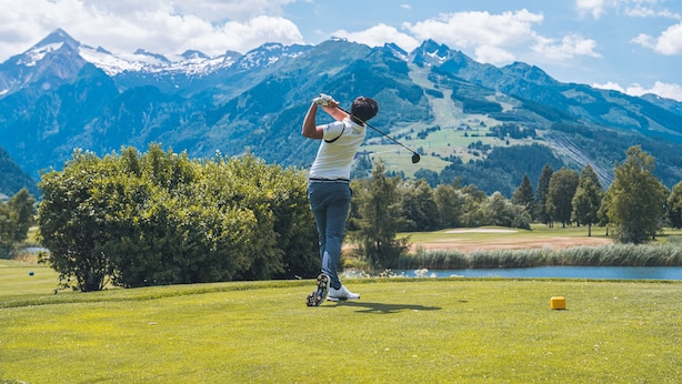A person playing golf on a well-maintained course with a lake and mountains in the background. - Living Schönwies (Zell am See)