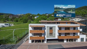 A modern multi-story building with balconies, surrounded by greenery and a clear sky. - Living Schönwies (Zell am See)