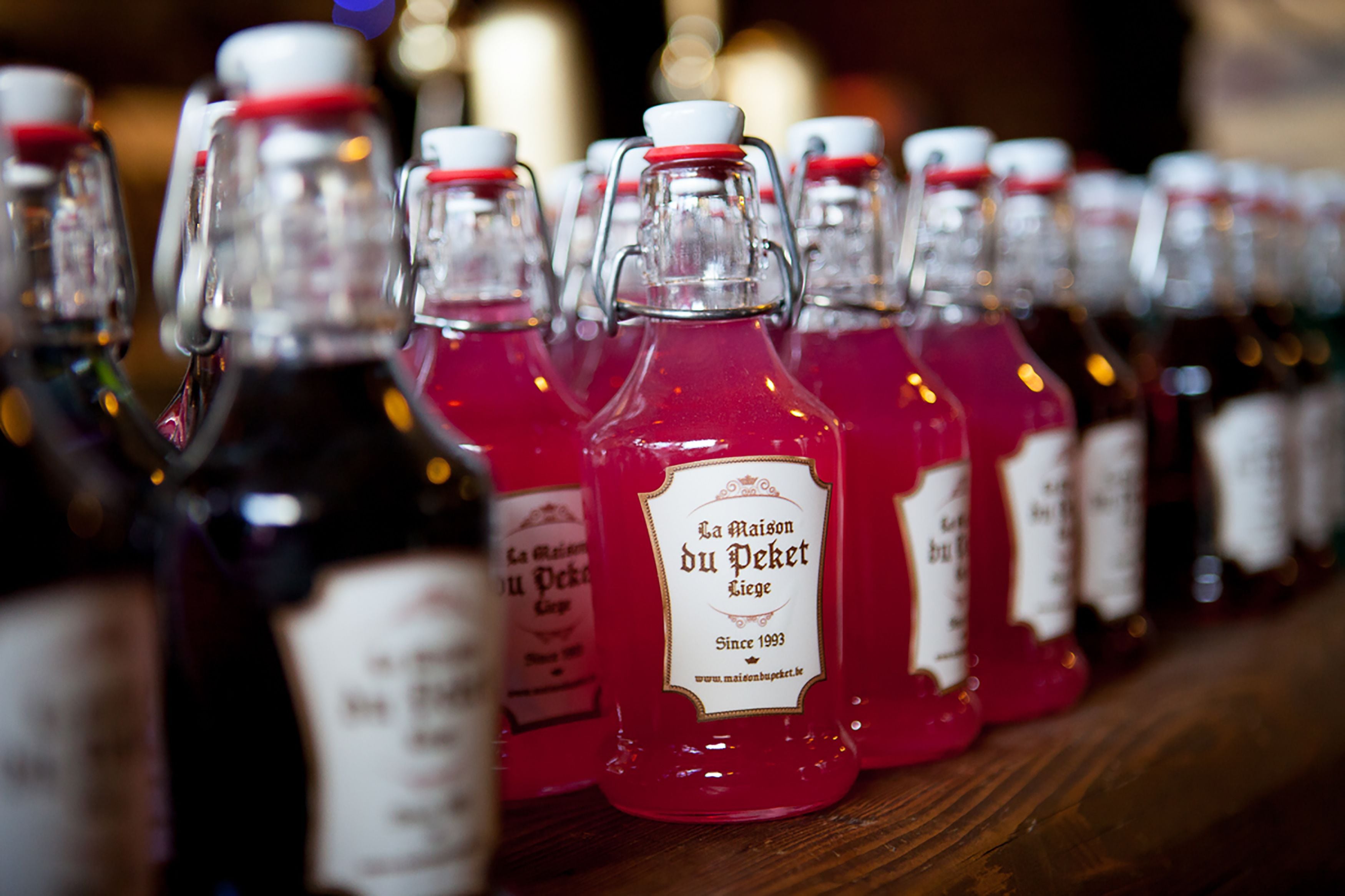 Una fila de botellas con etiquetas, algunas con líquido rojo visible.