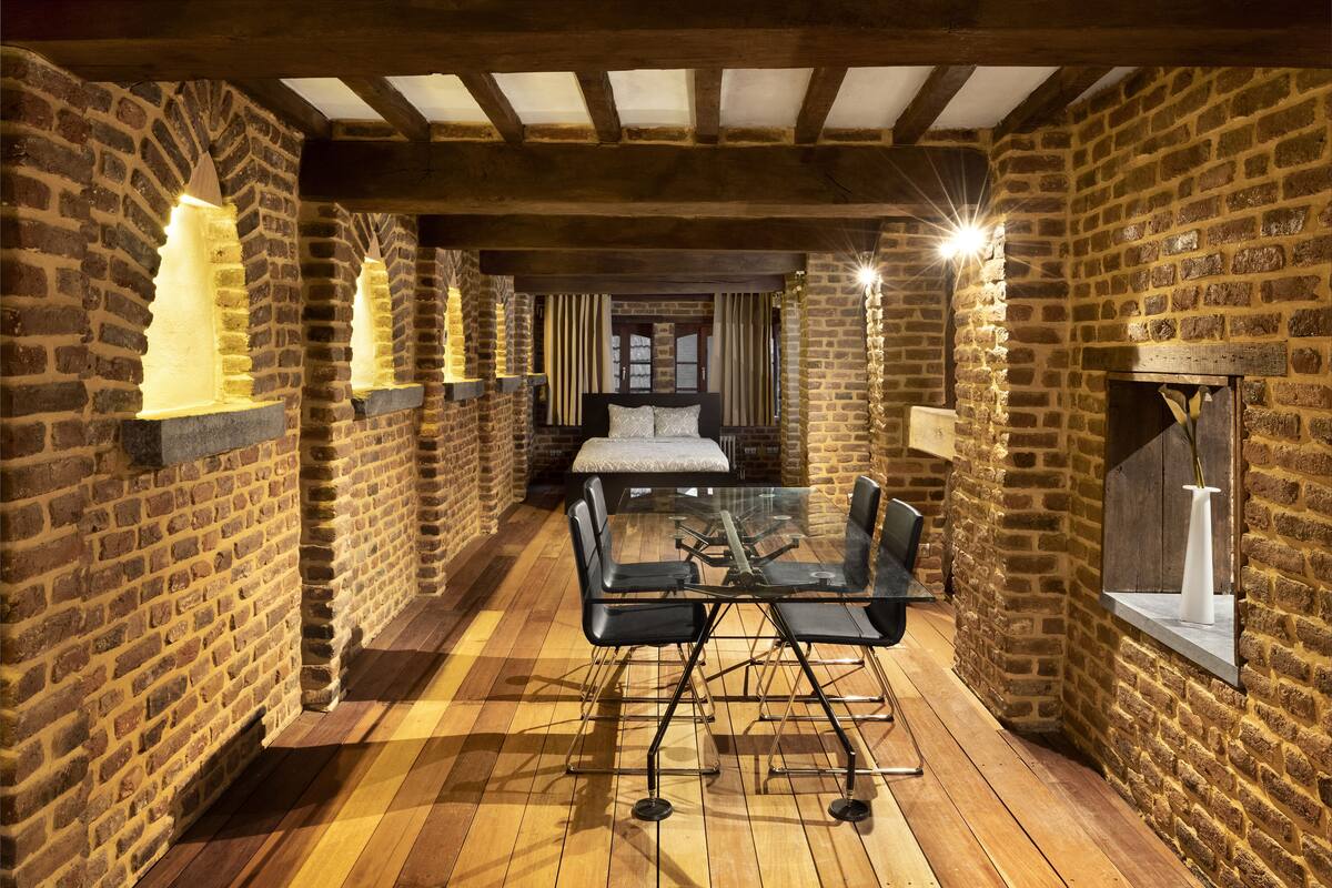 A room with a glass table and chairs, brick walls, wooden beams, and hanging lights.