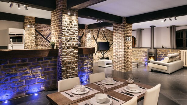 A modern kitchen with a stone wall, a fireplace, and a dining area with a table set for two. - Appart-Hotel Léopold Liège Centre (Liege)