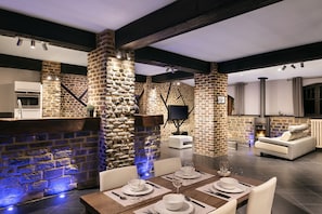 A modern kitchen with a stone wall, a fireplace, and a dining area with a table set for two. - Appart-Hotel Léopold Liège Centre (Liege)