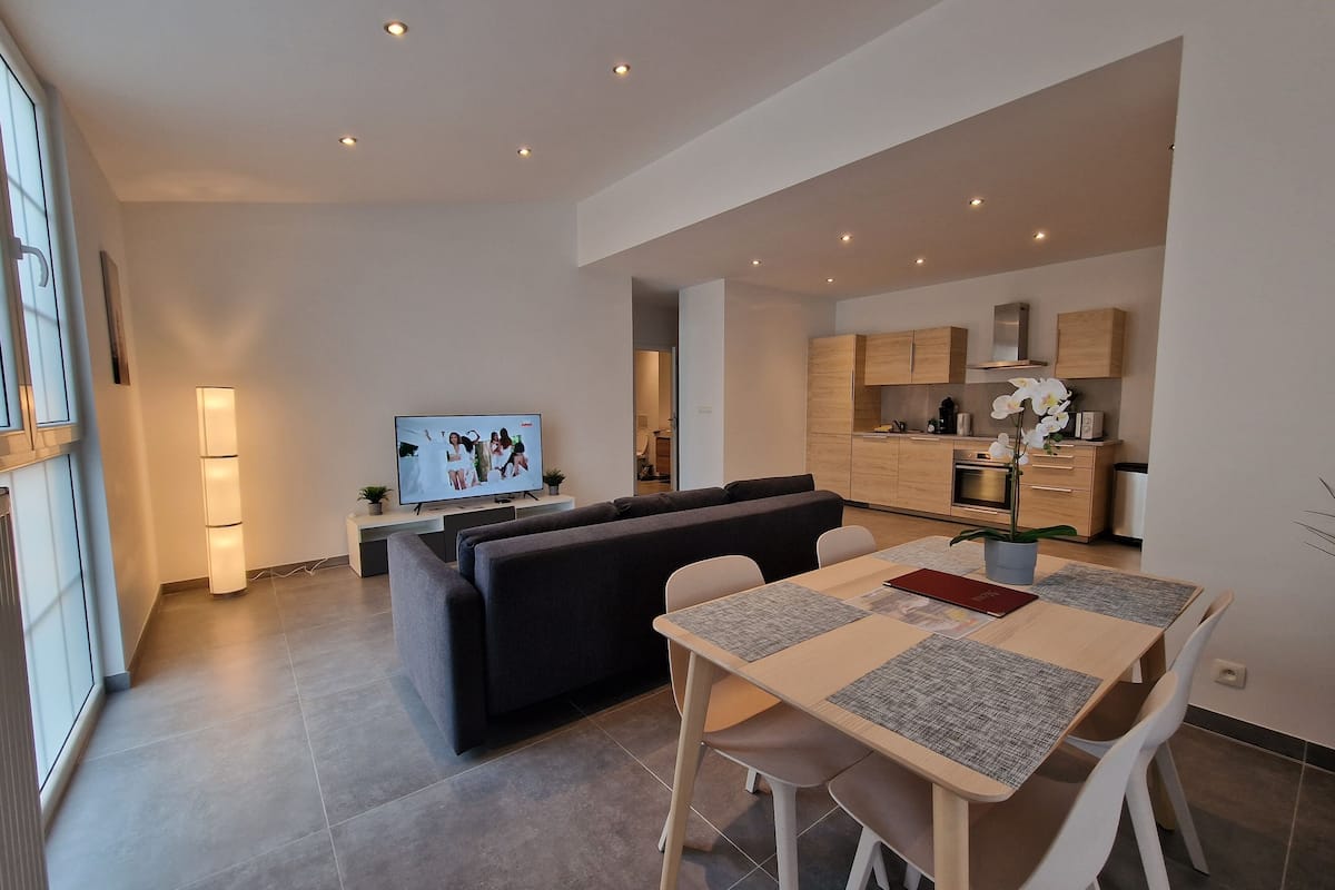 A modern living room with a sofa, dining table, and kitchen in the background.