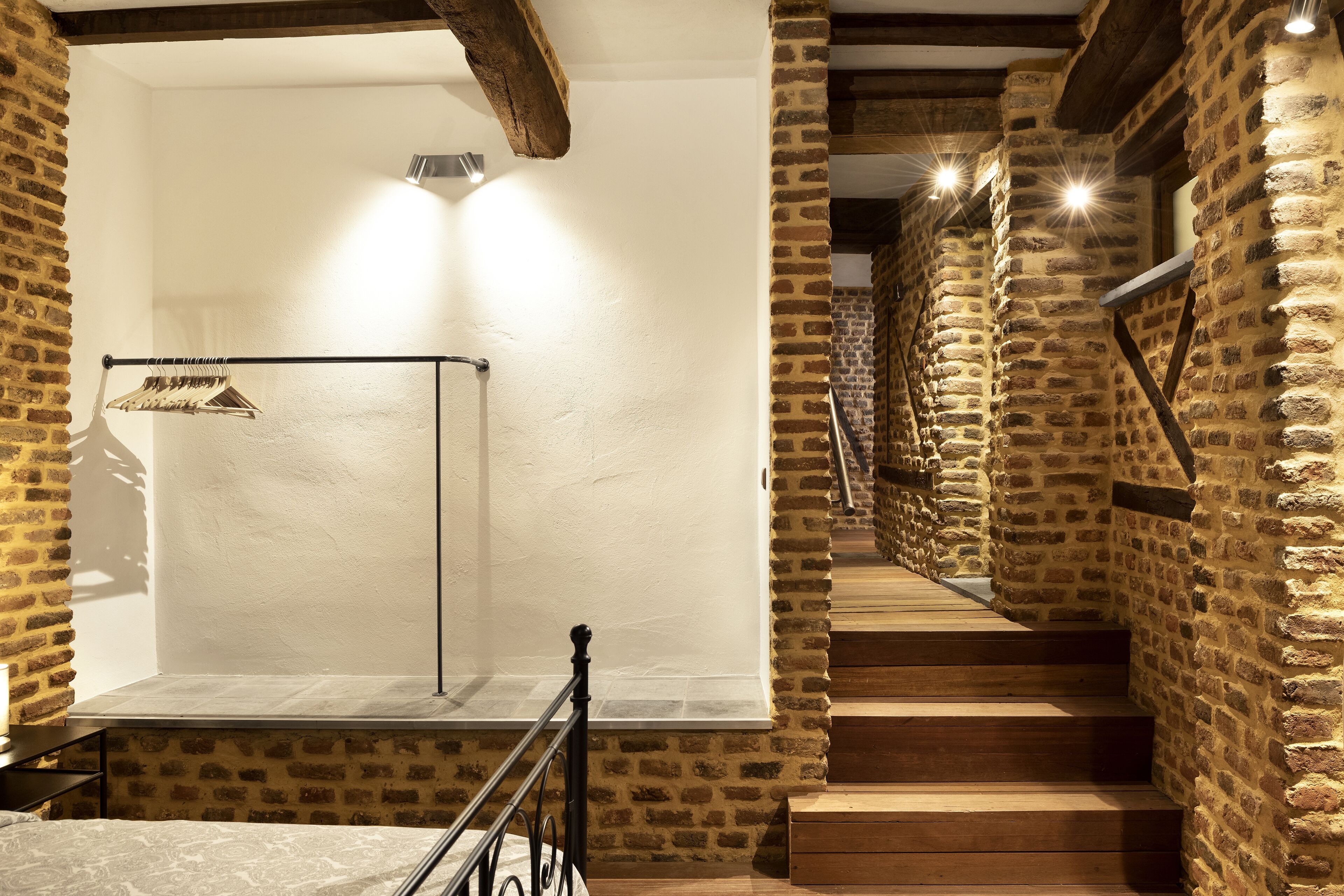 Una escalera de madera con paredes de piedra que conduce a una plataforma con un perchero metálico y una prenda colgada.