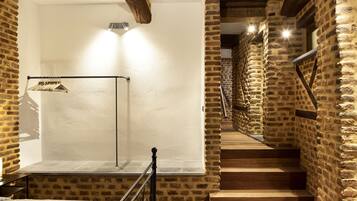 Una escalera de madera con paredes de piedra que conduce a una plataforma con un perchero metálico y una prenda colgada.