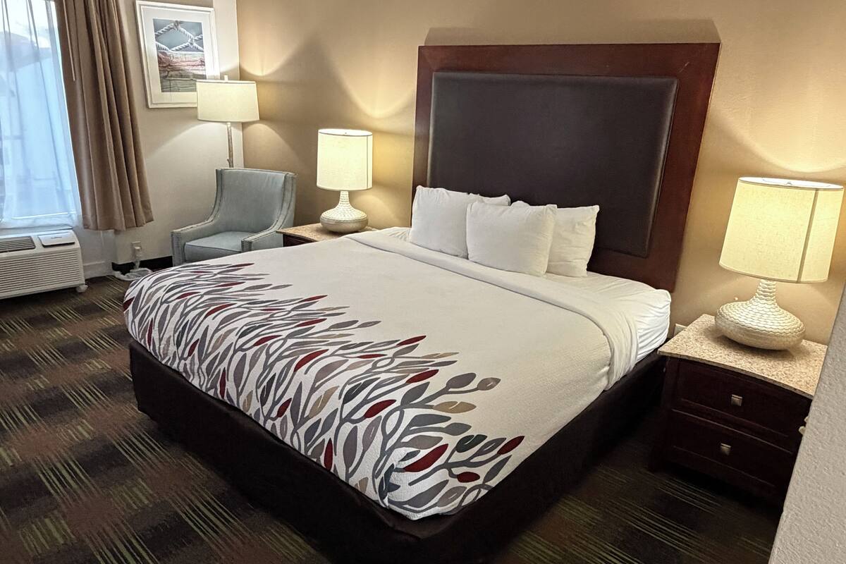 Quarto de hotel com uma cama grande, uma cadeira, uma escrivaninha e um abajur.