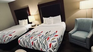 Hotellihuone, jossa on kaksi sänkyä, tuoli, lamppu ja pieni pöytä.