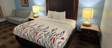 A hotel room with a bed, two bedside lamps, a nightstand, a sofa, and a framed picture on the wall.