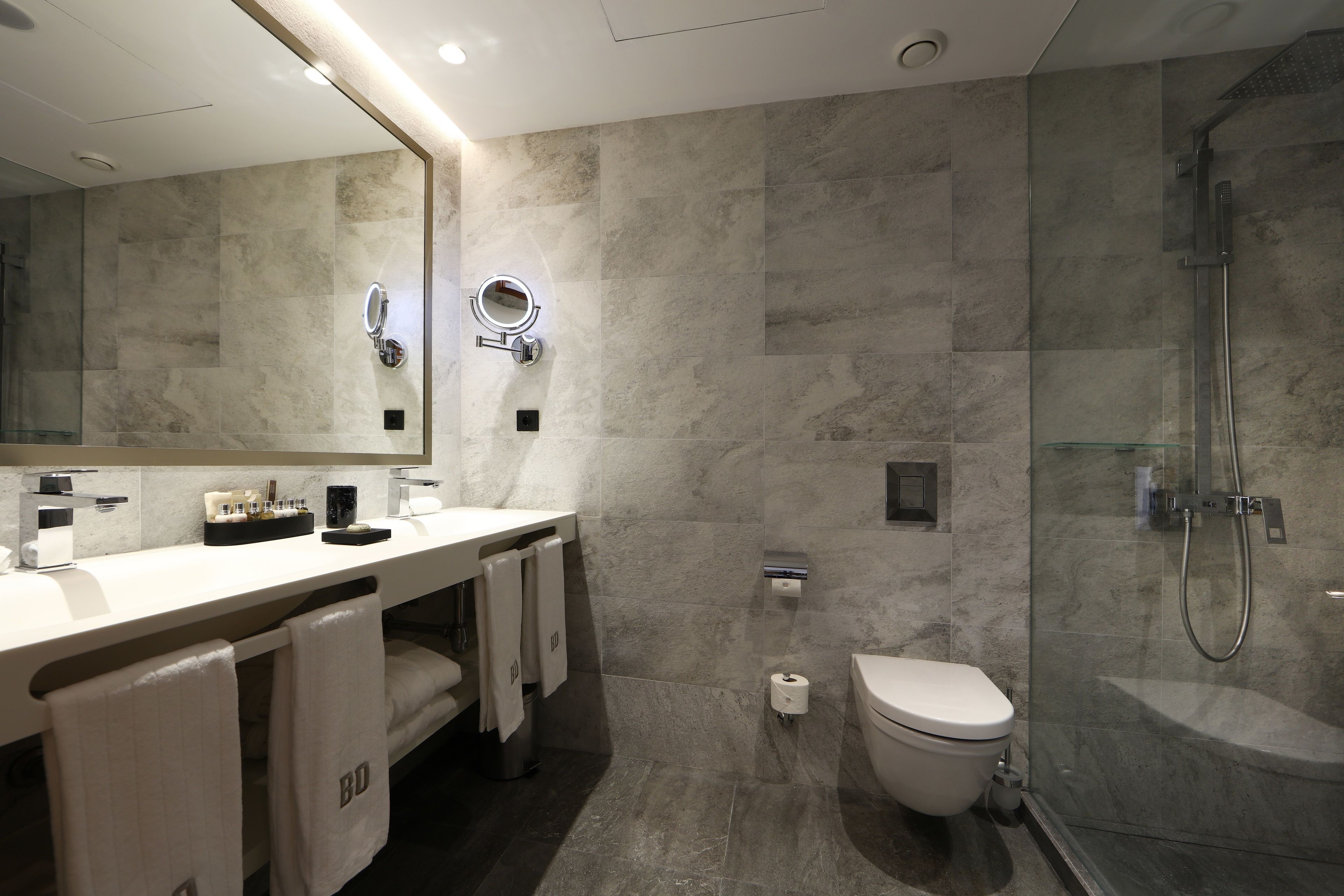 Un baño moderno con ducha de vidrio, inodoro y tocador con espejo y toallero.