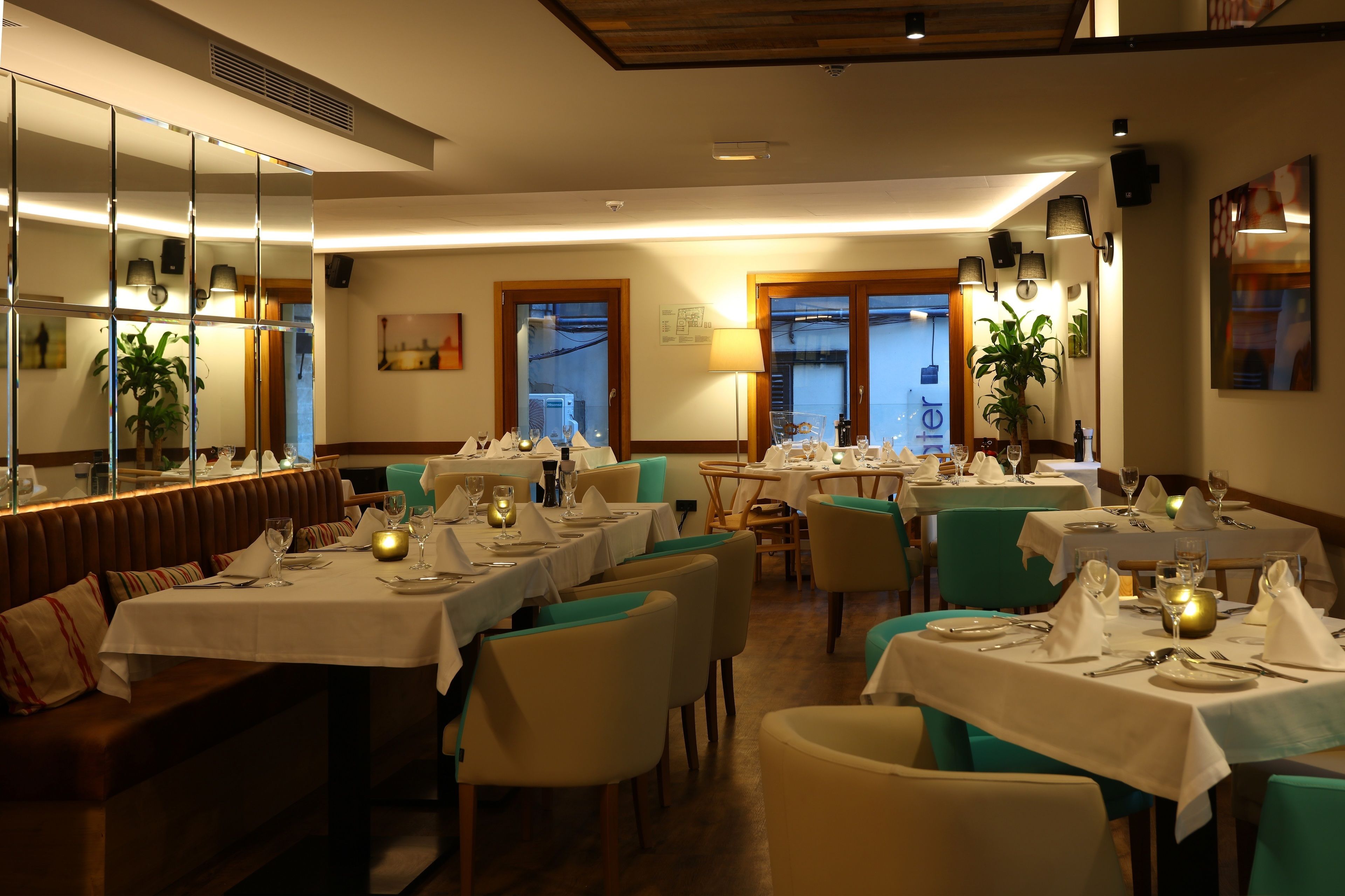 Un restaurante con varias mesas dispuestas para comer, que presenta un interior cálido con detalles de madera y sillas color turquesa.