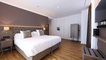 Una camera d'albergo moderna con un ampio letto, lampade ai comodini, un armadio, una TV a schermo piatto e una scrivania con una sedia.